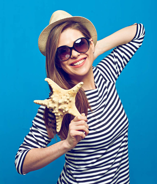 Smiling woman wearing striped shirt, sunglasses and hat holding starfish. Summer sea vacation concept. - Фото, зображення