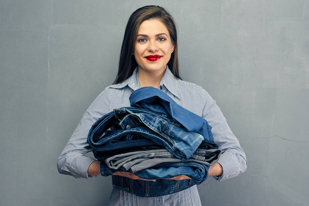 Portrait of young woman holding heap of denim pants. - Foto, afbeelding