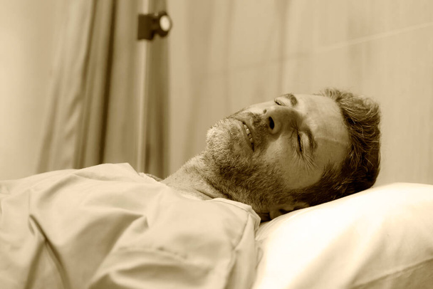 dramatic artistic hospital portrait of attractive and scared man infected by covid19 -  adult male in face mask receiving treatment for coronavirus respiratory desease on bed - Photo, image