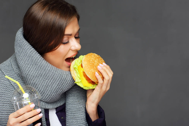 Portrait of woman wearing warm scarf eating fast food. Isolated on gray. - Fotoğraf, Görsel