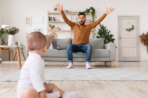 Divertido padre jugando con el bebé sentado en el sofá en casa - Foto, Imagen