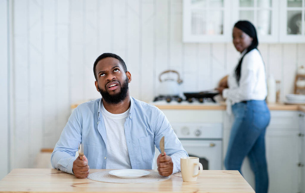 せっかちな空腹の黒人の夫は空のプレートで夕食を待って、退屈している - 写真・画像