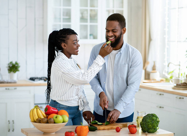 Kochająca czarna kobieta karmi męża podczas gotowania razem w kuchni - Zdjęcie, obraz