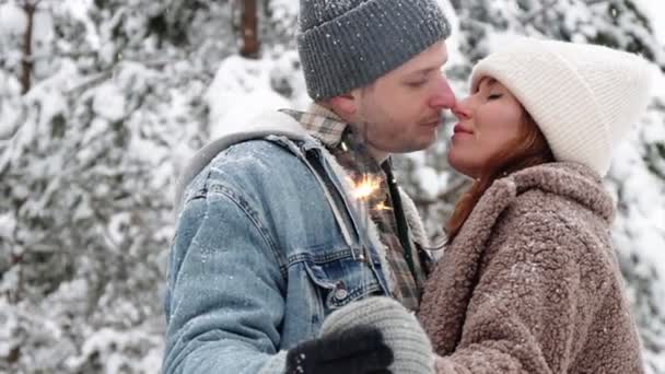 αγάπη, ευτυχία και ειδύλλιο έννοια - χαριτωμένο ζευγάρι ποζάρουν με sparklers και φιλιά στο δάσος του χειμώνα - Πλάνα, βίντεο