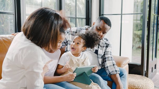 Young African American family and daughter happy using tablet at home. Mom, Dad, and child relax with little girl watching movie on sofa in living room. Funny parent and lovely child are having fun. - Fotoğraf, Görsel