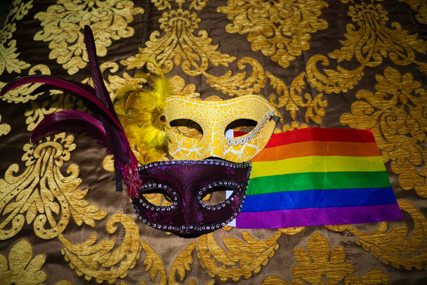 zwei Karnevalsmasken, eine lila und eine gelb auf barockem Hintergrund und Gay Pride Flagge - Foto, Bild