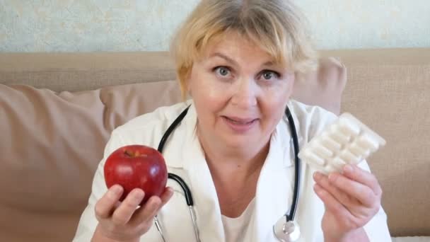 Retrato del médico dando manzana y pastillas en ampolla, frutas vs medicamentos, primer plano - Metraje, vídeo