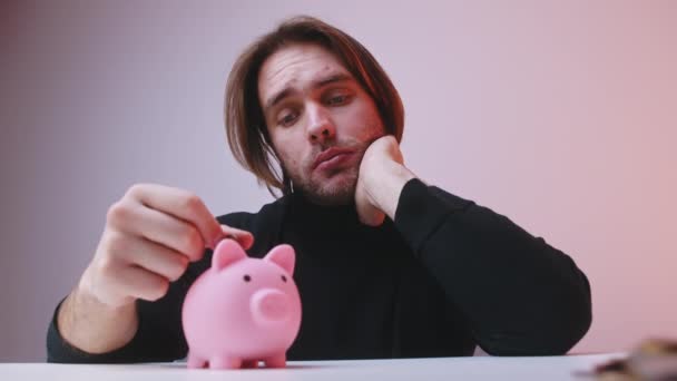 Jovem chateado homem colocando pequena quantidade de moedas no banco porquinho - Filmagem, Vídeo