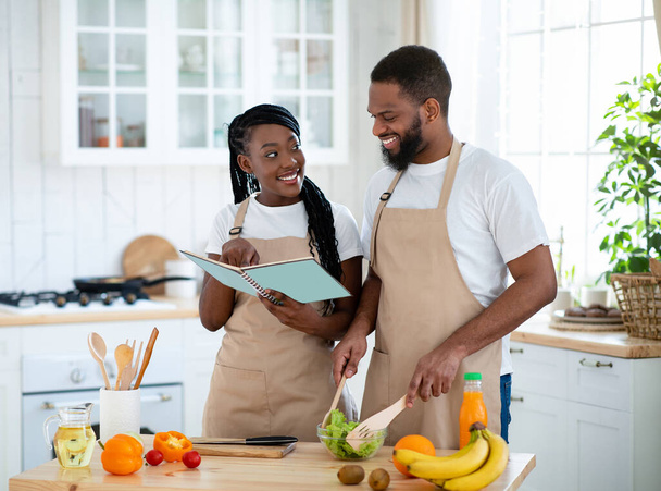 Happy Black Couple Checking Recipe In Cookbook While Cooking Together In Kitchen - Photo, Image