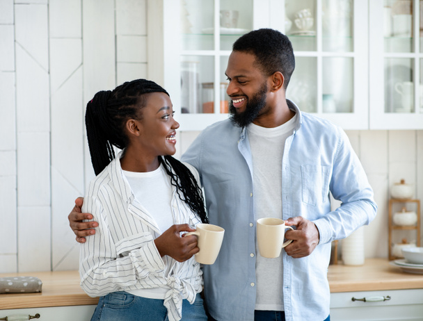 若いアフリカ系アメリカ人のカップルの笑顔キッチンでモーニングコーヒーを一緒に飲む - 写真・画像