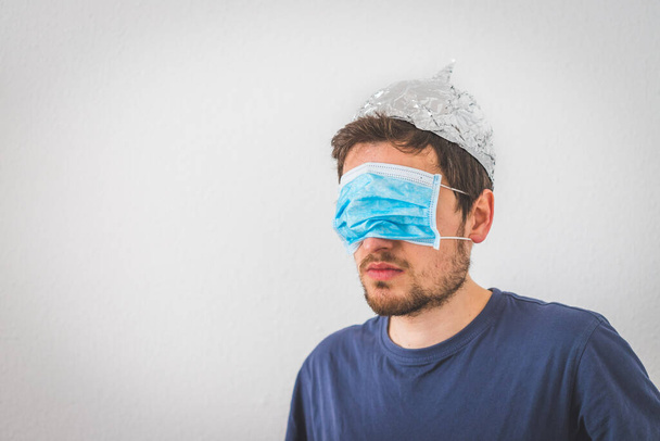 Young angry man with aluminum cap and face mask. Conspiracy theory concept. - 写真・画像