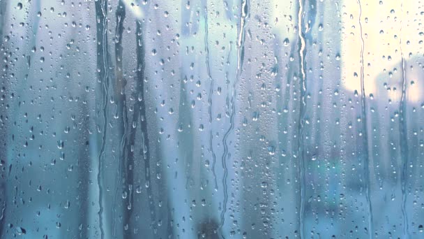 Spatten waterdruppels op het glas. Raam op een regenachtige dag.Nat glas met grote druppels water of regen. Video van waterdruppels op een helder glasoppervlak tijdens hevige regenval. Druipend water - Video