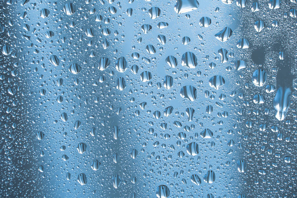 Dešťové kapky na sklo v deštivém počasí.Lesklý lesklý povrch vody na skle.Kapky vody ve formě kuliček nebo kuliček.Modré kapky deště pozadí. Abstraktní pozadí ornament s vodou - Fotografie, Obrázek