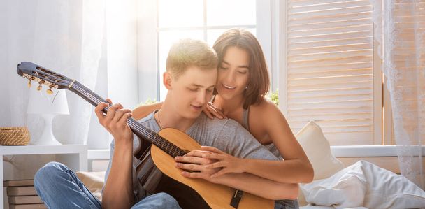 Happy couple in love. Stunning sensual portrait of young stylish fashion couple indoors. Young man playing guitar for his beloved girl. - Fotoğraf, Görsel