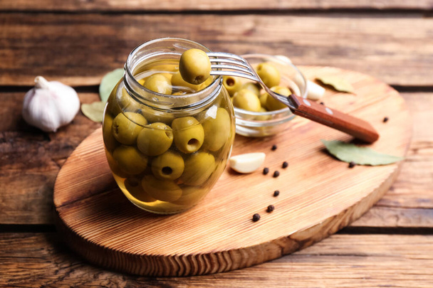 Glass jar of pickled olives on wooden table - Foto, afbeelding