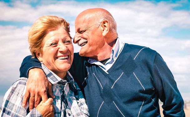Happy senior couple in love enjoying time together - Joyful elderly lifestyle and retirement concept with man whispering on woman ear - Bright warm vivid filter - Photo, Image
