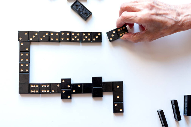 Entretenimiento familiar para un divertido juego de ocio de dominó. La mano de una anciana pone un dominó sobre la mesa. - Foto, Imagen