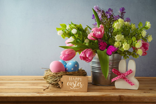 Easter holiday concept with easter eggs in bird nest and beautiful tulip flowers bouquet on wooden table - Foto, immagini