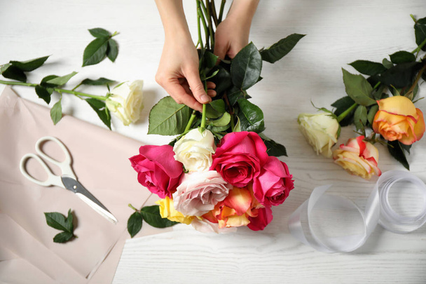 Woman making luxury bouquet of fresh roses at white wooden table, top view - Foto, Bild