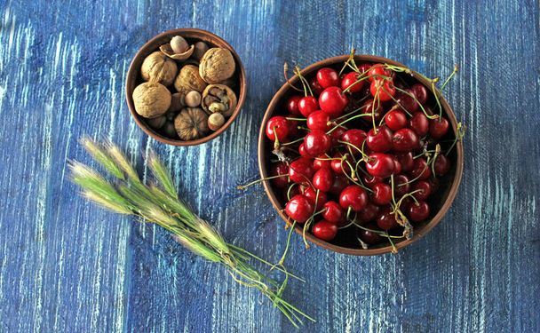 Čerstvé červené sladké třešně a vlašské ořechy v misce na dřevěném modrém stole - Fotografie, Obrázek