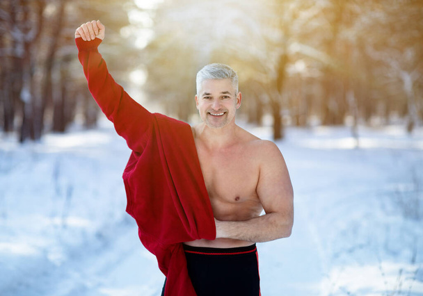 Entrenamiento de exposición en frío y concepto de aclimatación. Feliz hombre maduro quitándose la ropa de abrigo en el parque de invierno nevado - Foto, Imagen