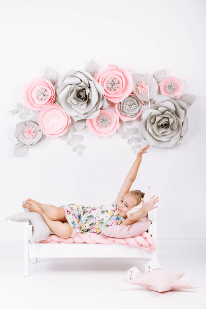 Ideje lefeküdni. A kislány korán kel. Puha ágy rózsaszín ágynemű fehér hálószobában kézzel készített virágokkal a falon.Gyermek alvási rend óra, napi rutin. Édes álmok koncepciója - Fotó, kép