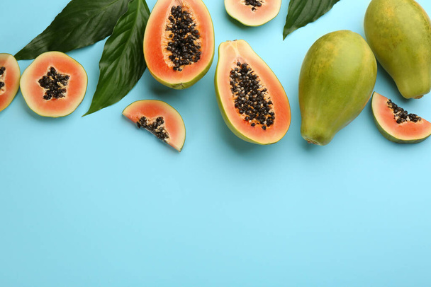 Fresh ripe papaya fruits with green leaves on light blue background, flat lay. Space for text - Zdjęcie, obraz