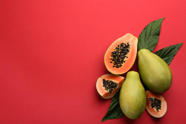 Fresh ripe papaya fruits with green leaves on red background, flat lay. Space for text - Фото, зображення
