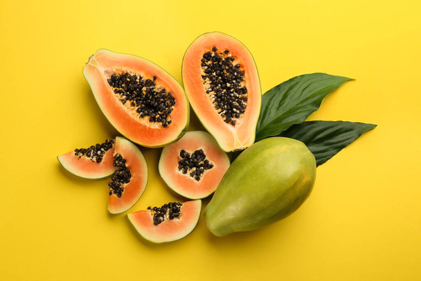 Fresh ripe papaya fruits with green leaves on yellow background, flat lay - Foto, Imagen