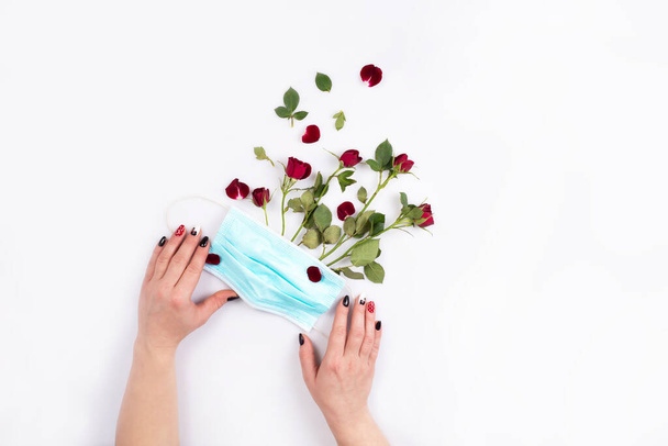 female hands holding a medical mask with a bouquet of roses. New reality ,life in a pandemia - Photo, Image