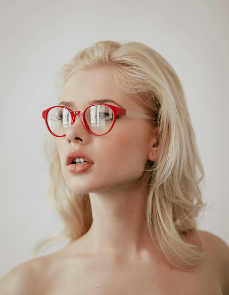 Closeup portrait of a sensual blonde woman with makeup wearing red eyeglasses, looking at the side, over white background. - 写真・画像