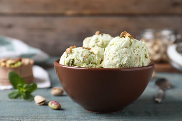 Delicious pistachio ice cream in bowl on blue wooden table - Foto, afbeelding