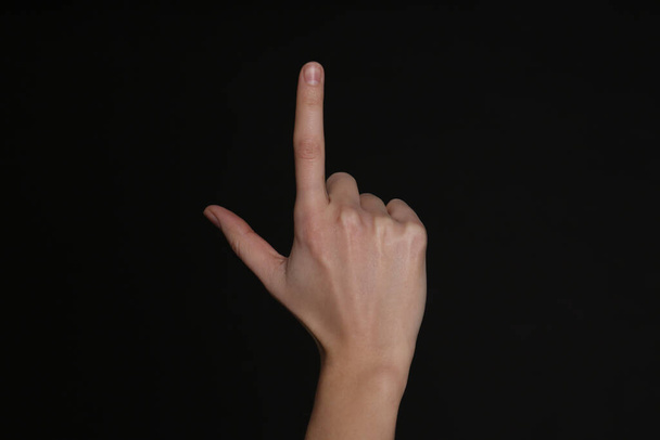 Woman pointing at something on black background, closeup. Finger gesture - Valokuva, kuva