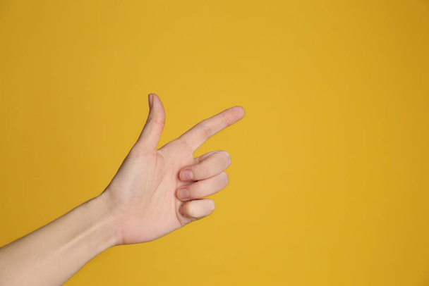 Woman pointing at something on yellow background, closeup. Finger gesture - Fotoğraf, Görsel