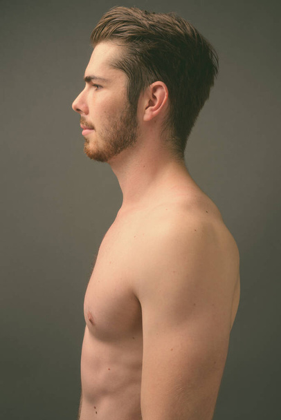 jovem bonito barbudo homem sem camisa contra cinza fundo - Foto, Imagem