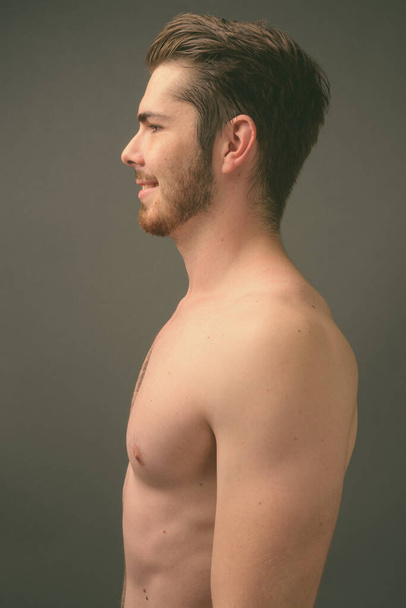 Νεαρός όμορφος γενειοφόρος άντρας χωρίς πουκάμισο σε γκρι φόντο - Φωτογραφία, εικόνα