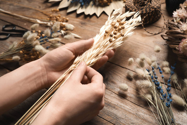 Florist making bouquet of dried flowers at wooden table, closeup - Foto, afbeelding
