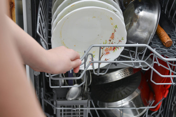 A háziasszony koszos edényeket tesz a mosogatógépbe, hogy mosson és takarítson az ételből.. - Fotó, kép