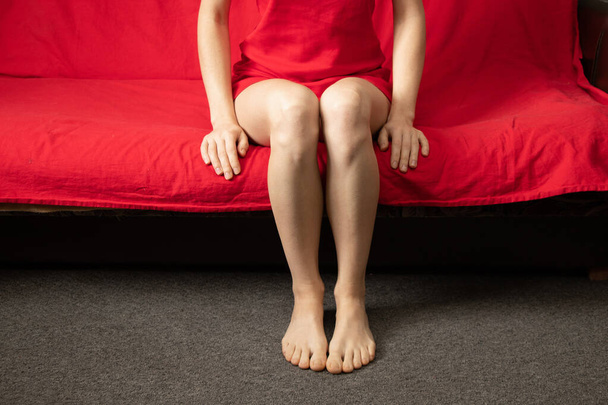 Nuori tyttö istuu paljain jaloin punaisella sohvalla kotona lomalla - Valokuva, kuva