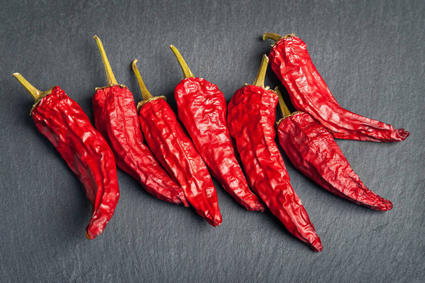 Red pepper. Dry peppers are spread out on a black slate stone. Hot chili peppers. Spices for cooking. - Photo, Image