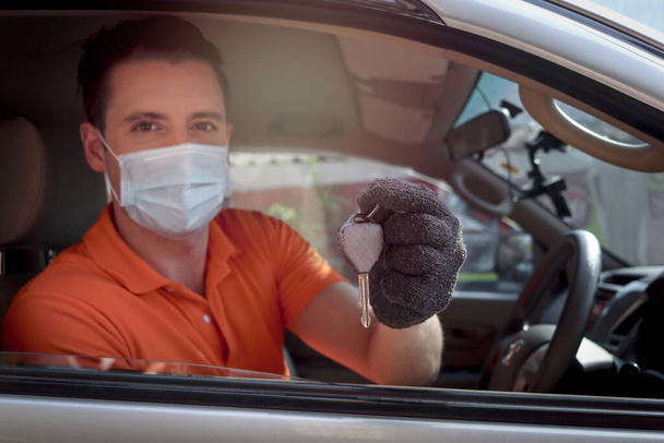 Young man with face mask holding a key in the car, auto mechanic driving customer car to automobile service center for checking and repairing. - Zdjęcie, obraz