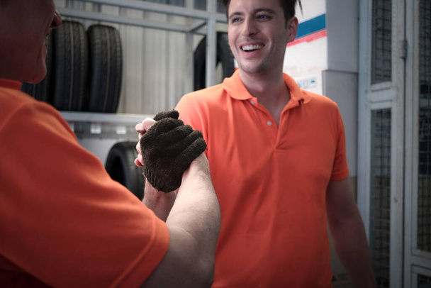 Dwóch wesołych i szczęśliwych pracowników daje dotykające ręce i hi pięć podczas pracy w warsztacie samochodowym centrum obsługi. serwis samochodowy pokazujący powitanie pracy zespołowej podczas wspólnej pracy. - Zdjęcie, obraz