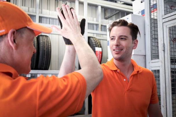 Dwóch wesołych i szczęśliwych pracowników daje dotykające ręce i hi pięć podczas pracy w warsztacie samochodowym centrum obsługi. serwis samochodowy pokazujący powitanie pracy zespołowej podczas wspólnej pracy. - Zdjęcie, obraz