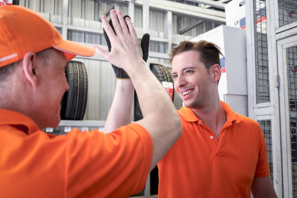 Dva veselí a šťastní dělníci, kteří se dotýkají rukou a hi-5 při práci v servisním centru garážových vozů. auto servisní technik ukazující týmovou práci pozdravy při spolupráci. - Fotografie, Obrázek