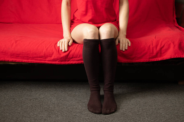 egy barna hosszú zoknis lány lábai, aki egy vörös kanapén ül vakáción, magányban. - Fotó, kép