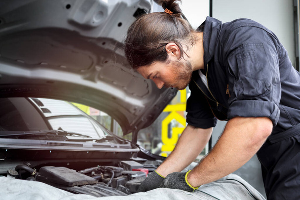 Auto mechanic working with engine in garage, car service technician repairing customer car at automobile service center, inspecting car suspension and engine system, vehicle repair service shop. - 写真・画像
