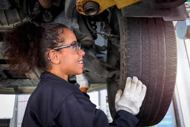 Female auto mechanic work in garage, car service technician woman check and repair customer car at automobile service center, inspecting car under body and suspension system, vehicle repair service shop. - 写真・画像