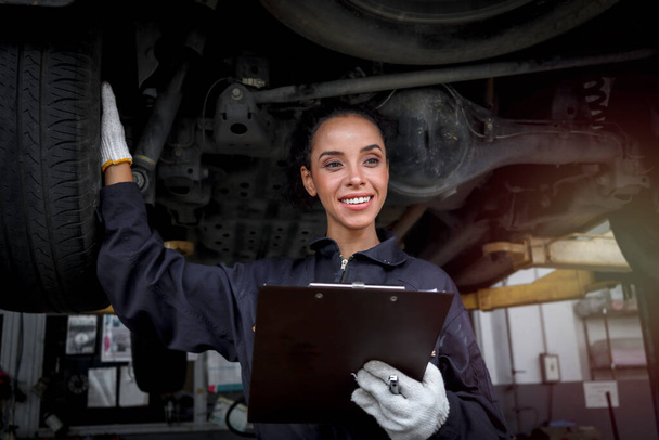 Female auto mechanic work in garage, car service technician woman check and repair customer car at automobile service center, inspecting car under body and suspension system, vehicle repair service shop. - Foto, Imagem
