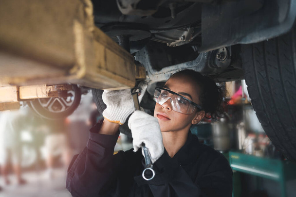 Female auto mechanic work in garage, car service technician woman check and repair customer car at automobile service center, inspecting car under body and suspension system, vehicle repair service shop. - Valokuva, kuva