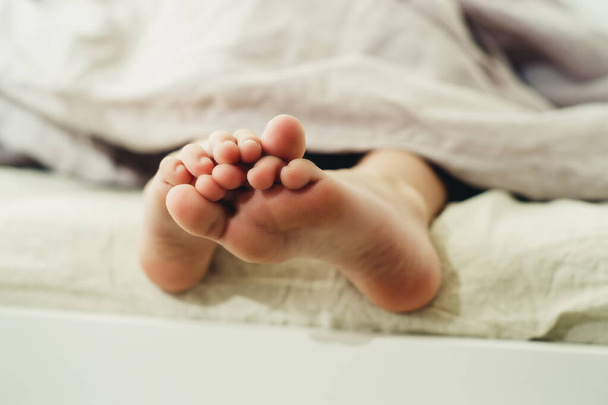 Kleine Füße unter einer hellen Decke in Großaufnahme - Foto, Bild